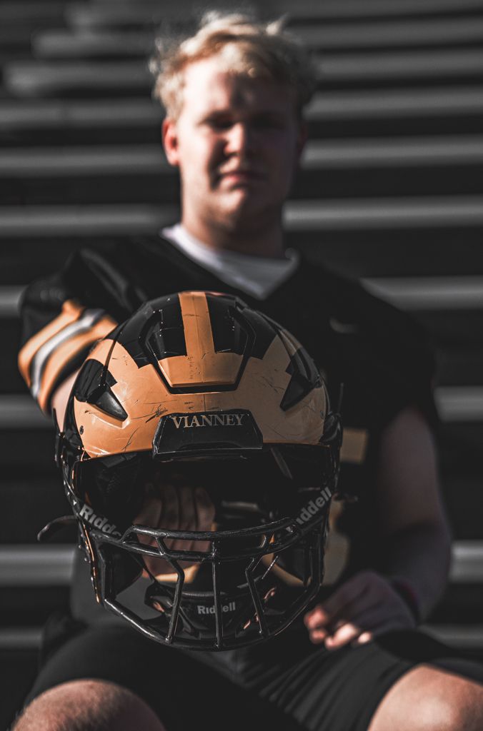 Senior portrait of high school football student in uniform holding his helmet in front of him.