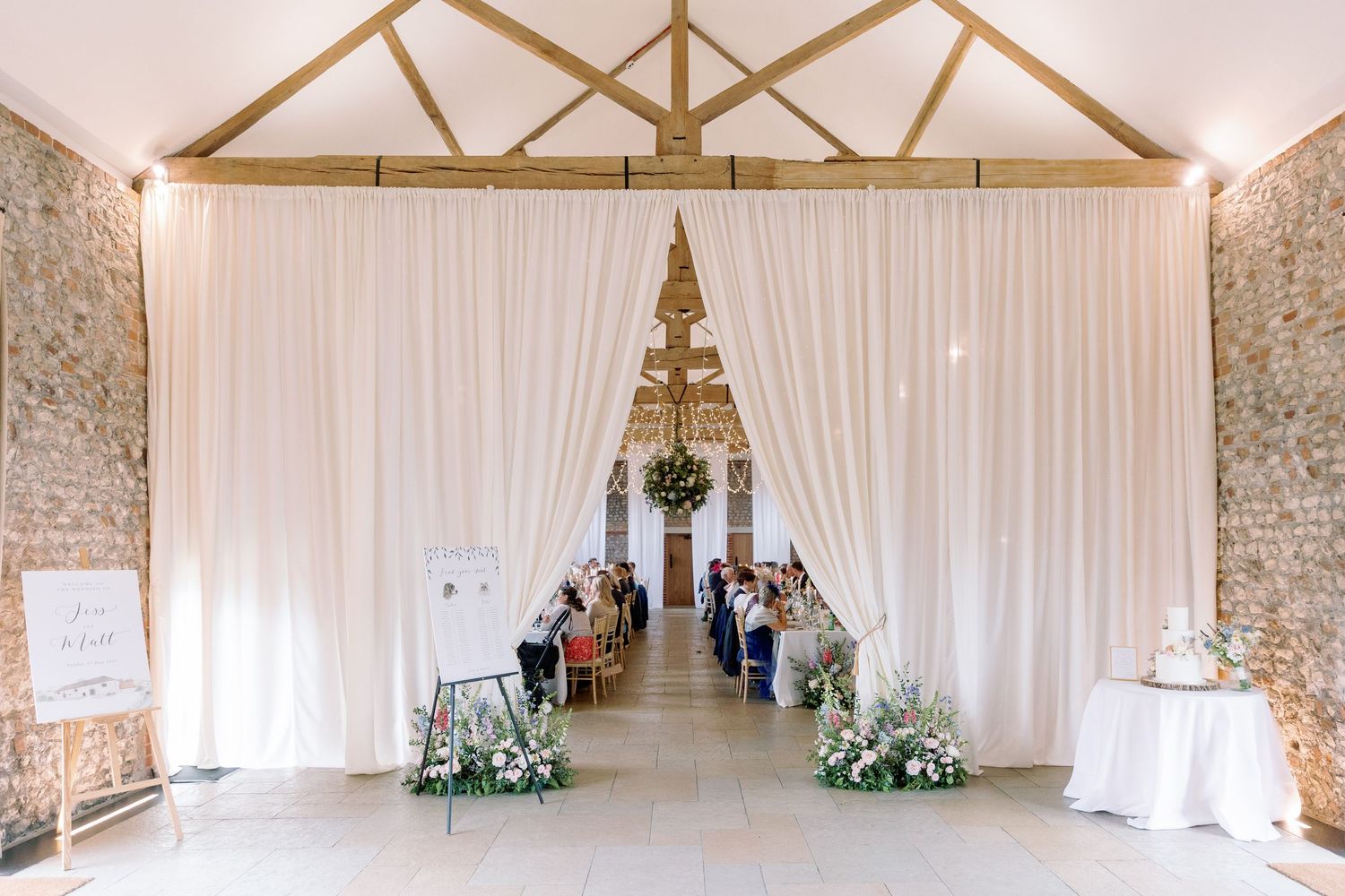 Rustic barn wedding venue interior with exposed wooden beams and white drapes creating an elegant ceremony space.