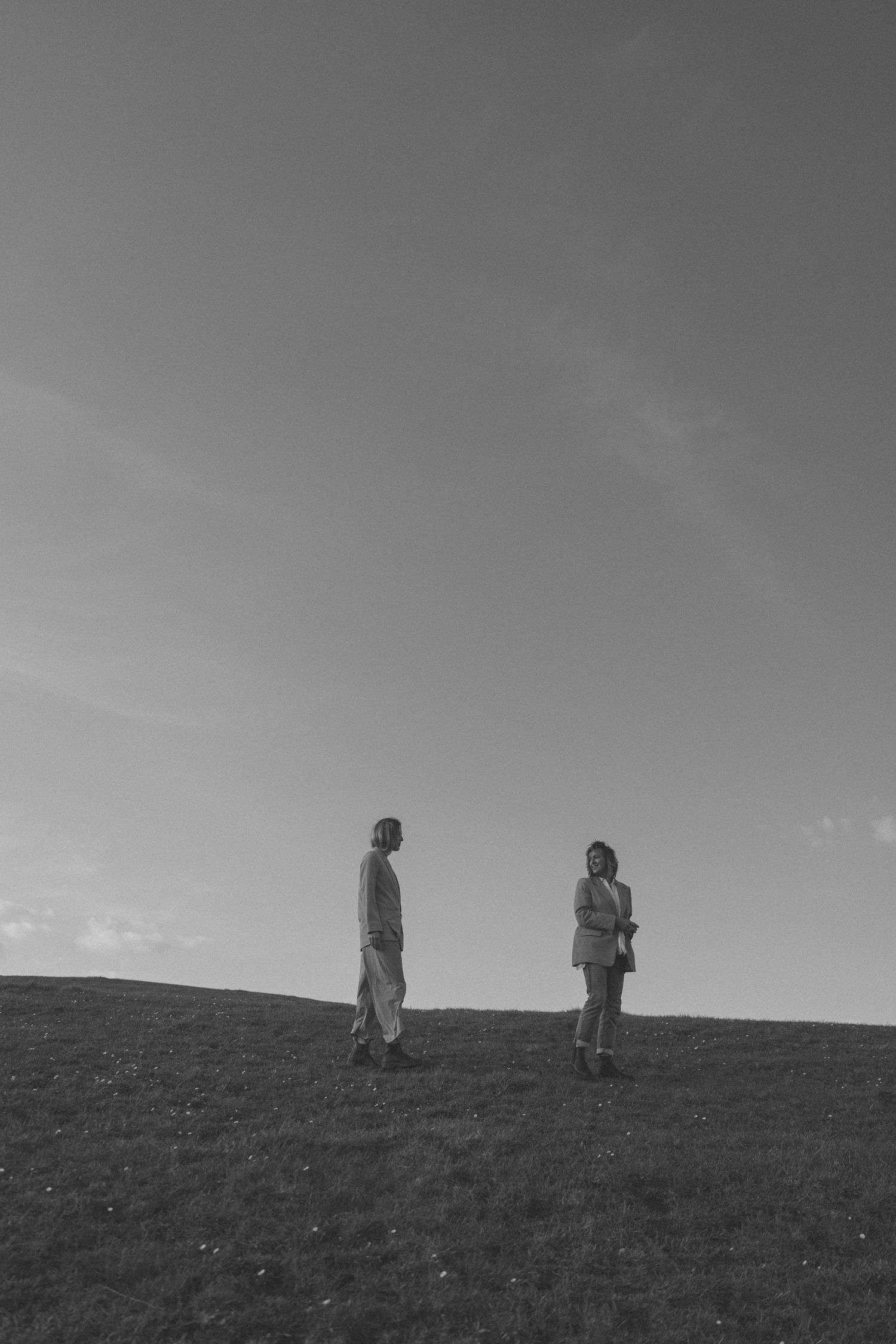 Black and white photo of two people standing apart on a grassy hill under a vast open sky in New Zealand.