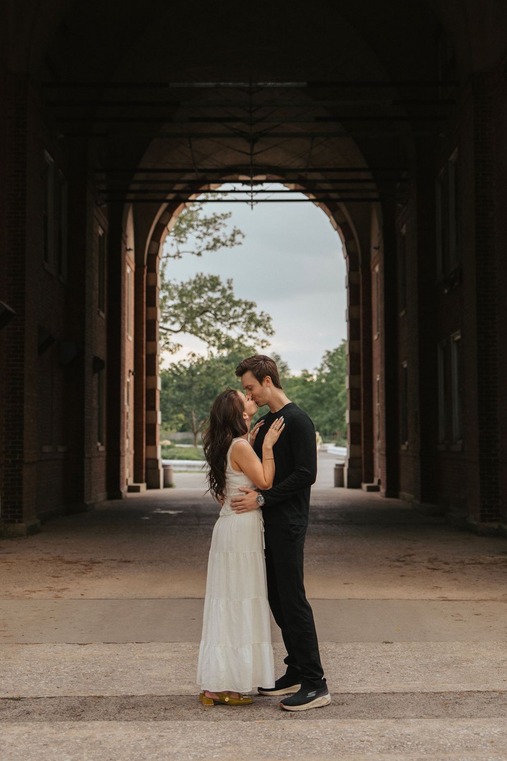 A romantic embrace captured under an arched passageway with natural lighting.