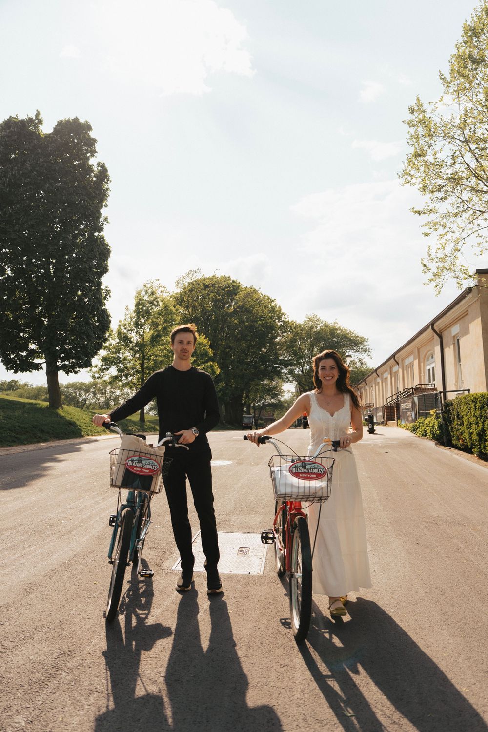 Couple with bicycles casting long shadows on residential street.