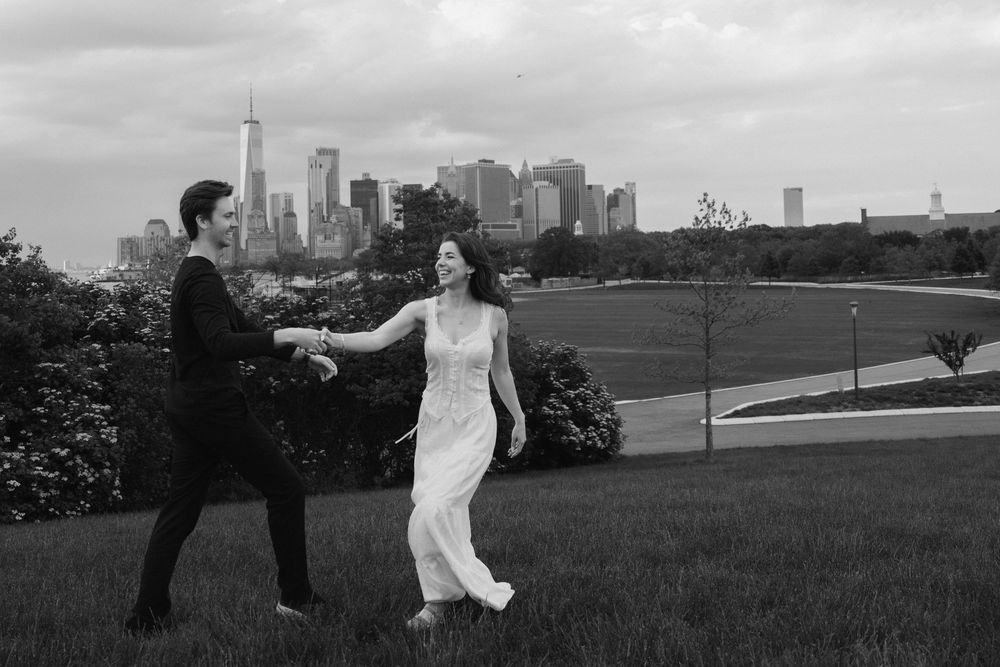 A couple dances together on a grassy hill with the New York City skyline visible in the background.