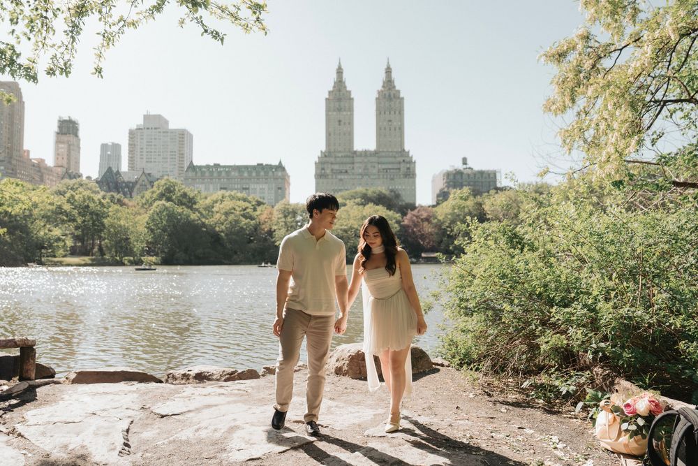 A couple walks hand in hand by a lake with the San Remo towers visible in the background.