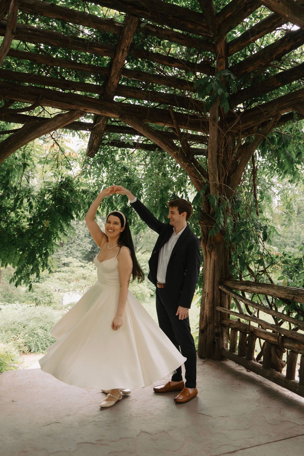 Dancing couple in formal attire beneath a wooden pavilion structure.