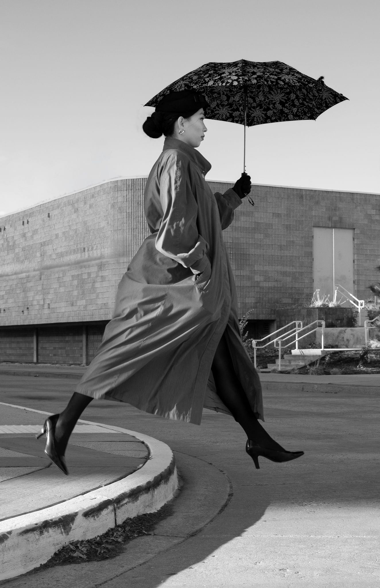 Black and white sequence of person with umbrella leaping gracefully across concrete surface.
