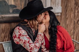 A romantic couple in western attire share an intimate moment against a rustic wooden backdrop.