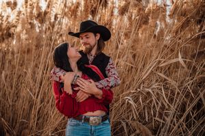 A couple embraces romantically among tall brown reeds during a golden hour photoshoot in the countryside.
