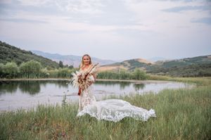 Woman in flowing dress poses gracefully by a serene mountain lake.