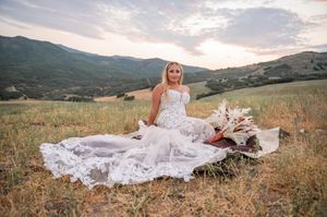Stunning mountain landscape with flowing white wedding dress train in golden field at sunset.