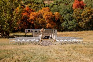 Outdoor wedding ceremony setup with white chairs and wooden arch against vibrant fall foliage backdrop.