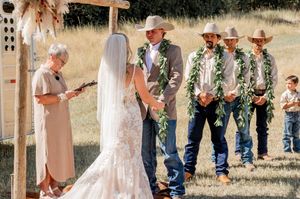 Country western themed wedding ceremony with cowboy-attired groomsmen under rustic arch.