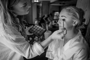 Black and white photo of makeup application during wedding preparations.
