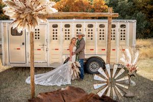 Rustic wedding reception setup with vintage decor, hay bales, and white portable restroom trailers in an outdoor setting.