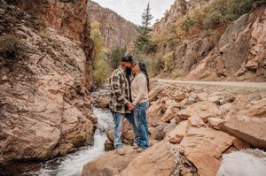 Rocky canyon trail with flowing stream and towering cliff walls in natural setting.