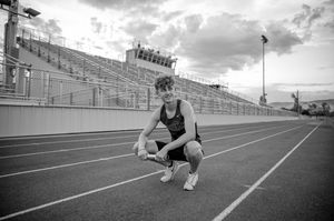 Runner crouches on an empty track with stadium bleachers in the background.