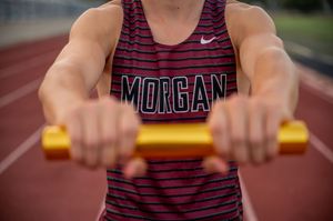Close-up of hands holding a yellow relay baton while wearing a Morgan track uniform.