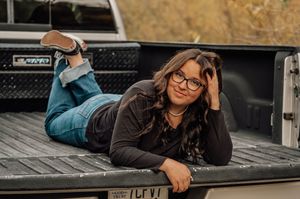 Casual pose on pickup truck bed with mountain scenery in background.