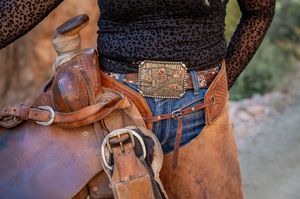 Western style belt buckle and leather saddle detail against denim.
