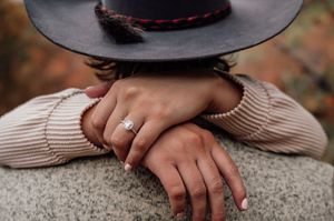 Close-up of hands wearing an engagement ring with a black hat in view.