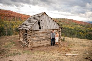 Old weathered wooden cabins against autumn mountain backdrop with cloudy skies.