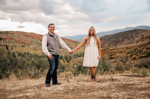 A couple holds hands while standing in an autumn mountain landscape at sunset.