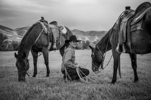 Black and white photo of horses and riders on a grassy field with mountains in the background.