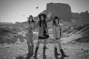 Three friends jump joyfully in black and white against a desert mountain backdrop.