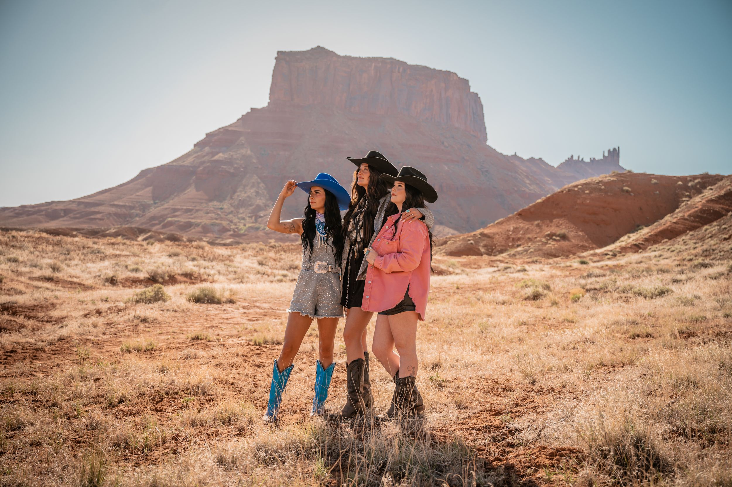 Two friends pose together in cowboy boots against a dramatic desert mesa landscape in the American Southwest.