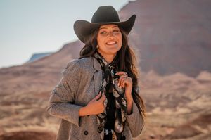 A photographer wearing a cowboy hat and gray jacket poses with camera equipment in the desert.