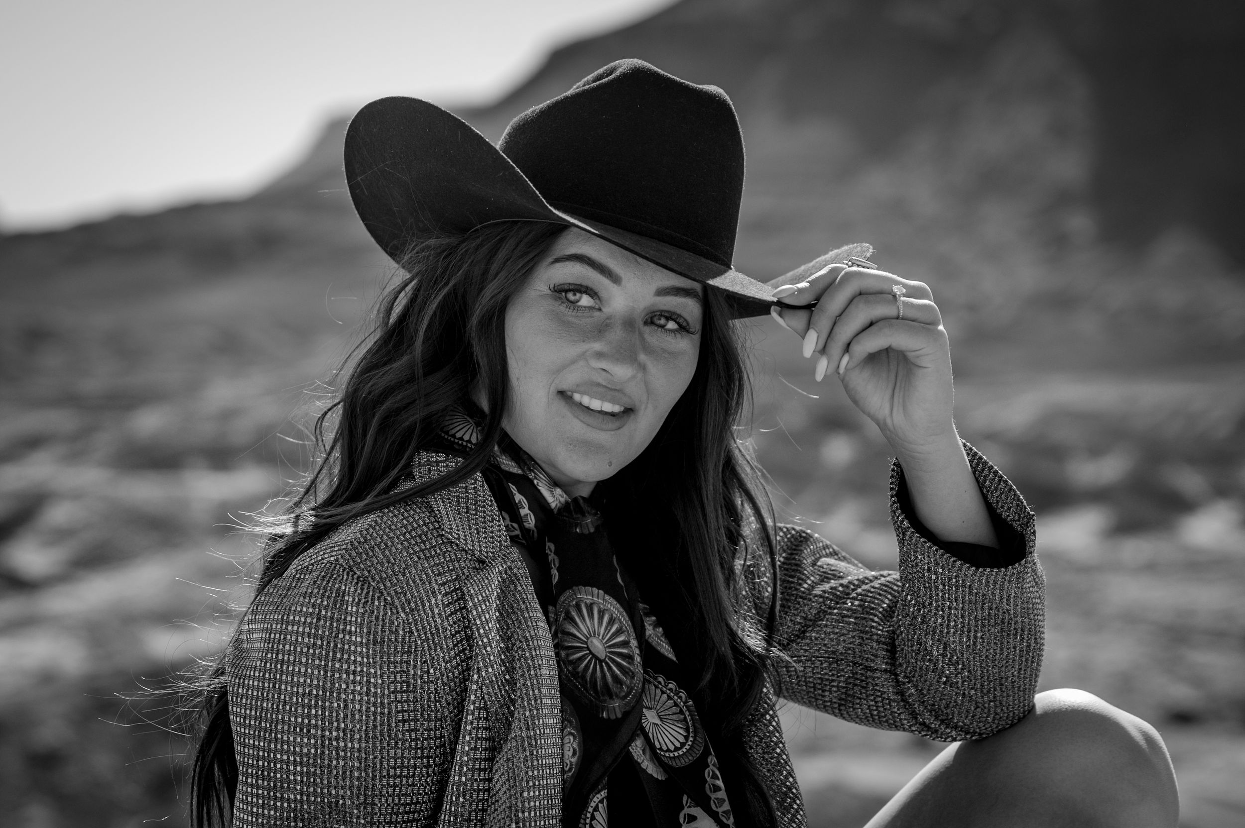 Black and white portrait of someone in western attire tipping their cowboy hat.