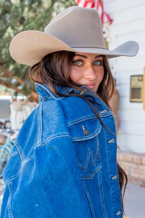 Person wearing denim jacket and beige cowboy hat in western style photoshoot.