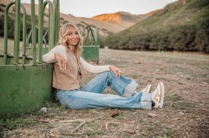 Casual outdoor portrait against green farm equipment with mountains in background.