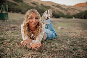 Casual outdoor portrait on grass with mountains in warm sunset lighting.