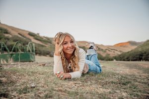 A casual outdoor portrait laying in grass with mountains in the background.