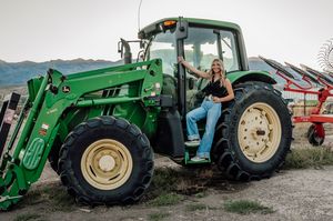 A green John Deere tractor with someone posing in casual attire on the steps.