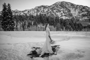 Black and white photo of bride in winter mountain setting with evergreen trees.