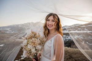 A winter bridal portrait with dried floral bouquet against snowy mountain backdrop.