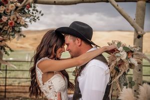Romantic outdoor wedding moment under a wooden arch decorated with pink flowers.
