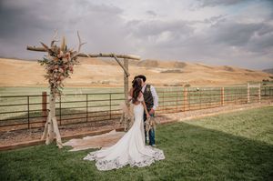 Outdoor wedding venue with rustic wooden arch and white draping against mountain backdrop.