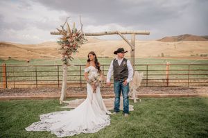 Rustic outdoor wedding setup with wooden arch and mountain views in background.
