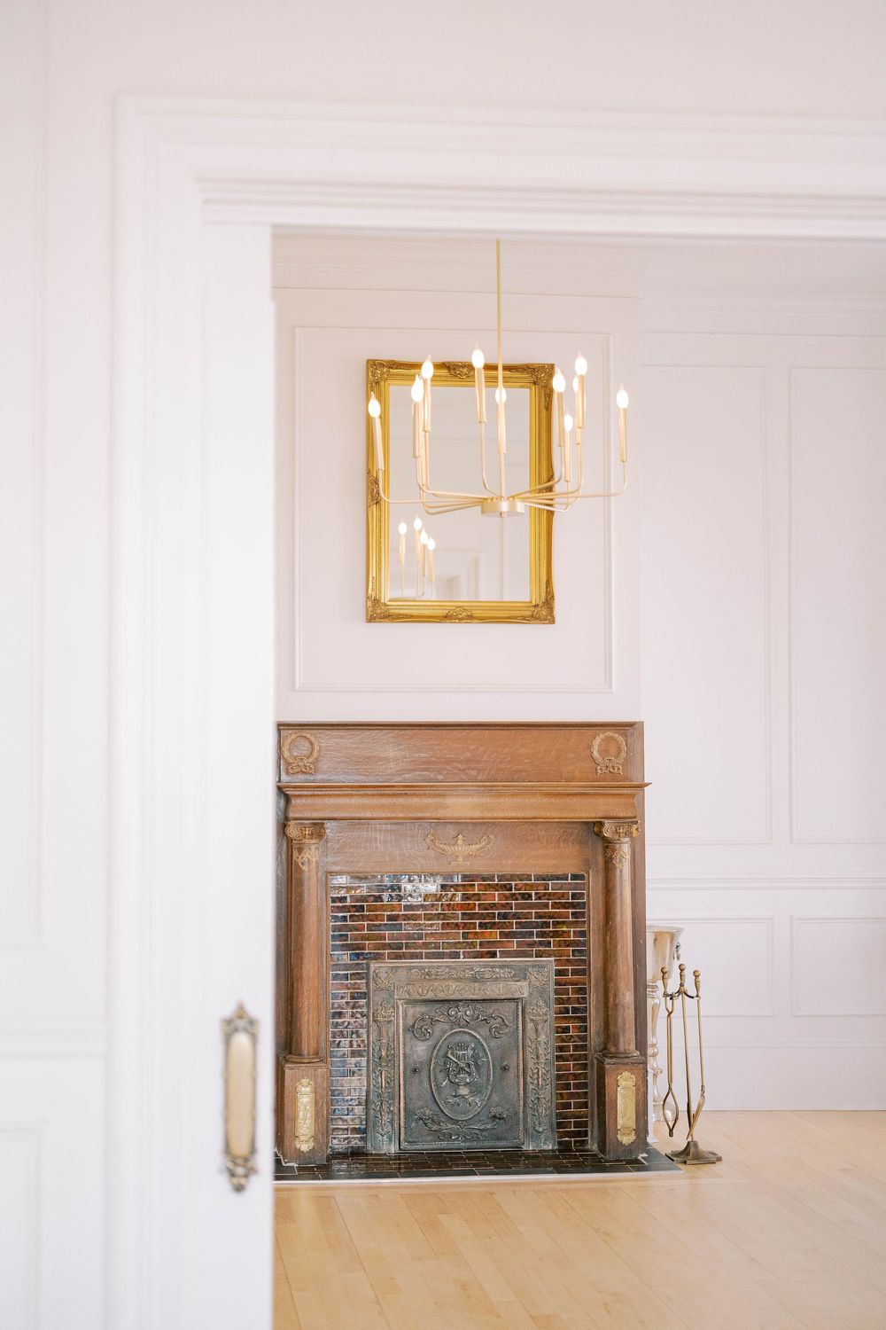 Elegant white room interior with brick fireplace, ornate molding, and gold-framed artwork above mantel.