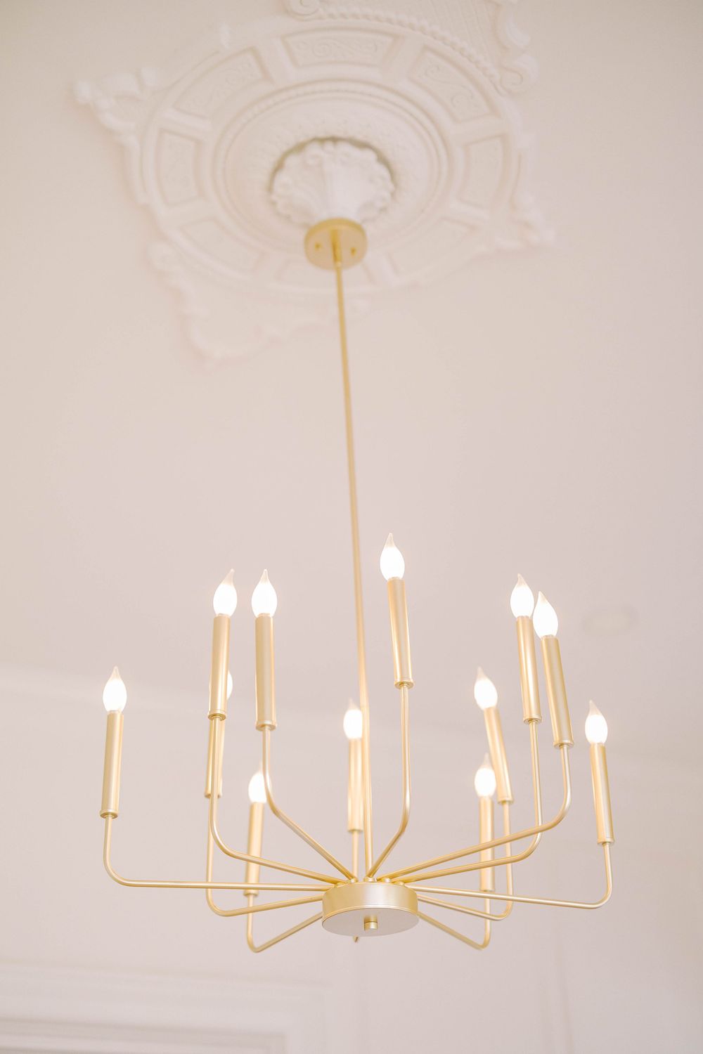 A series of three minimalist gold chandelier light fixtures with multiple arms shown against a light neutral background.