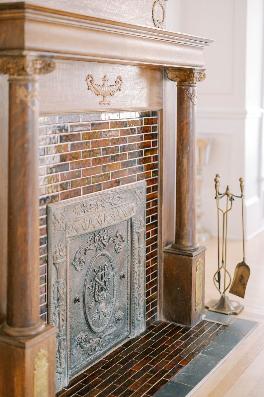 Ornate vintage fireplace with decorative wooden mantel, brick interior, and antique brass fire tools.