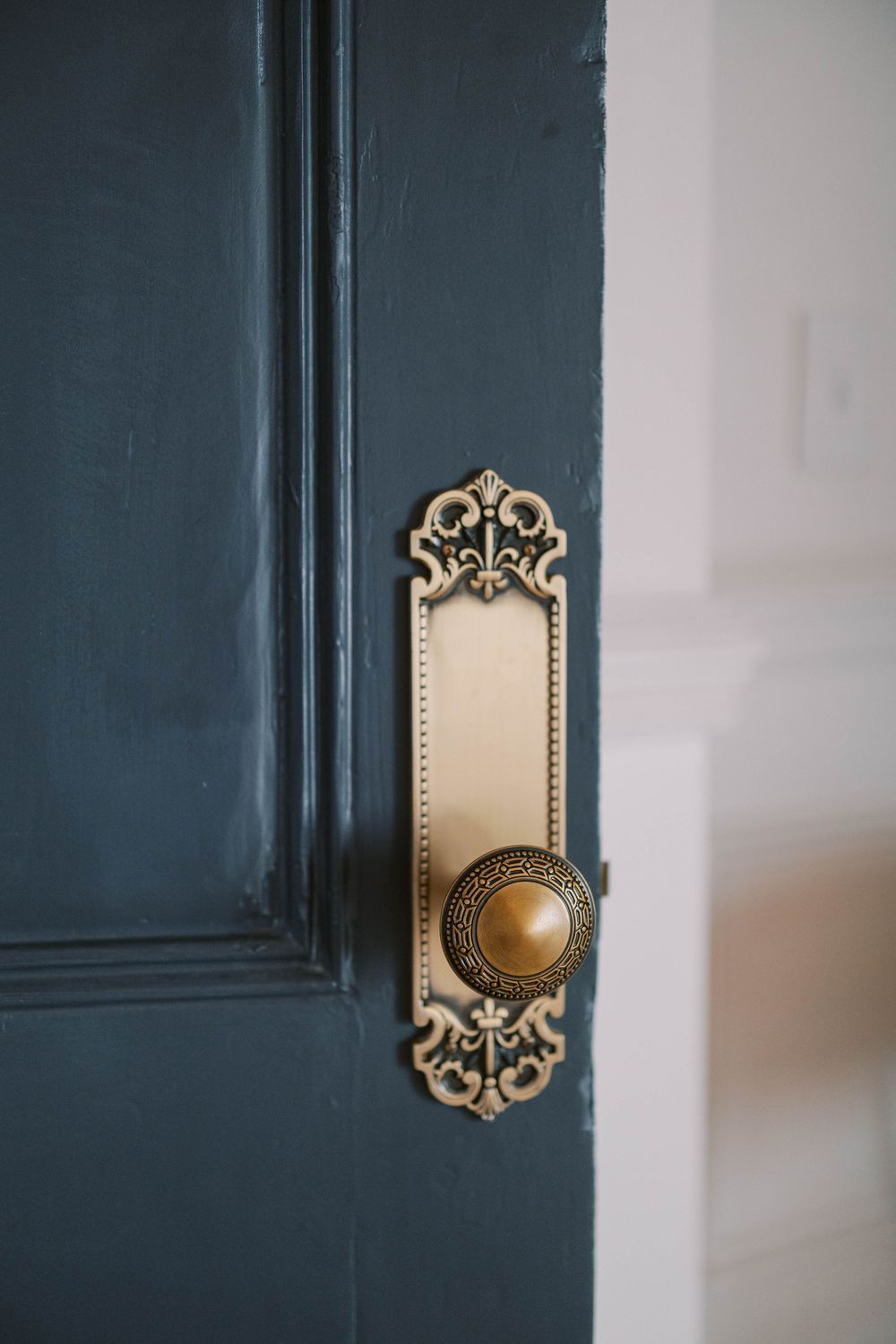 Ornate vintage brass door handles and decorative backplates mounted on dark teal painted doors.