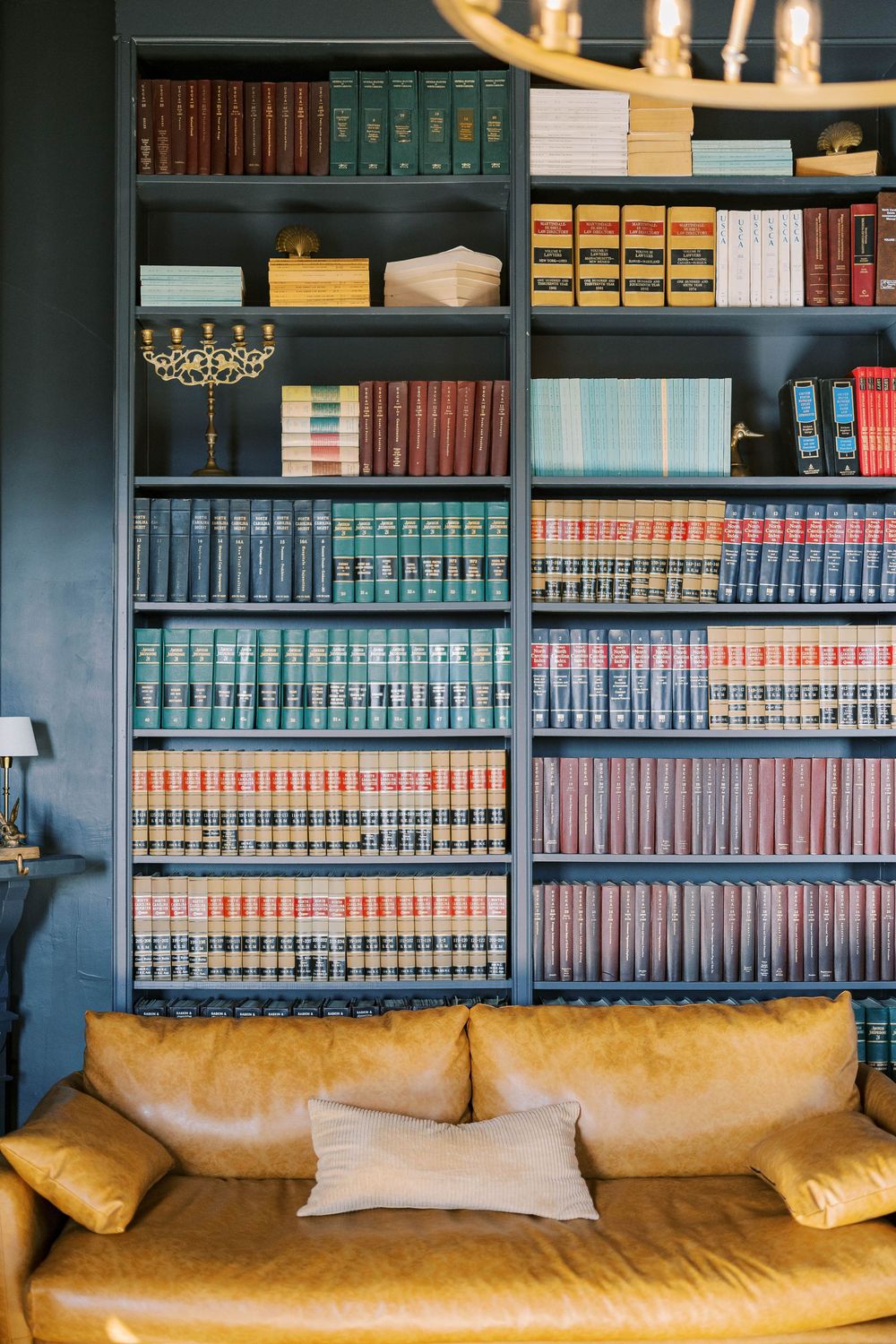 Floor-to-ceiling built-in bookshelf filled with colorful vintage books and tan leather couch below.