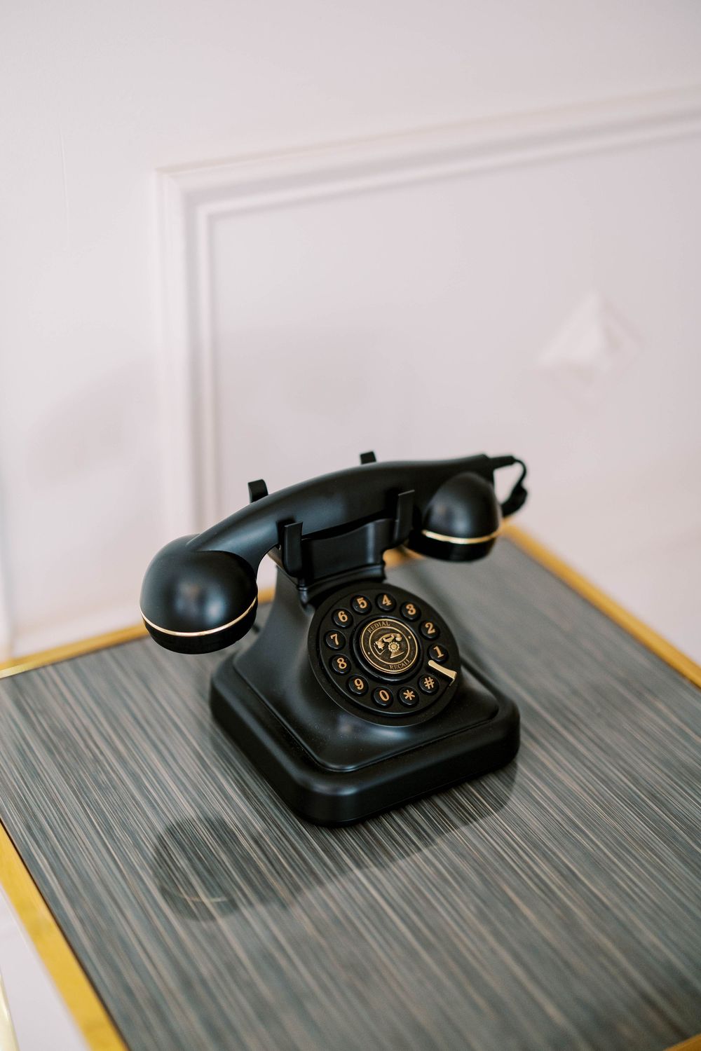 Vintage black rotary telephone sitting on a dark wooden surface against a white wall.