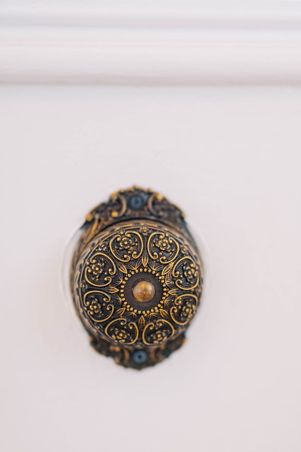 Vintage-style ornate brooch with intricate black and gold filigree pattern and pearl center.