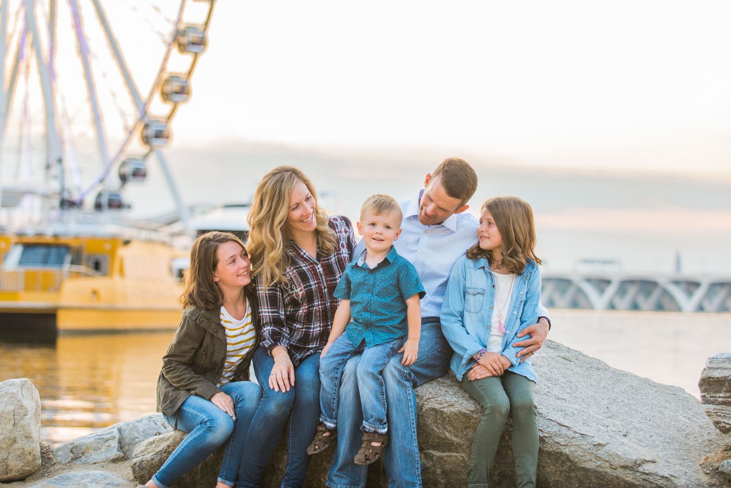 Family sitting together on rocks near a waterfront during sunset.