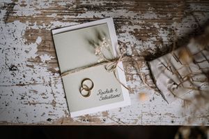 Invito di nozze con anelli dorati e fiori secchi su superficie rustica in legno in stile vintage.