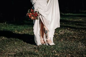 Un primo piano dei piedi di una sposa con scarpe bianche che regge un bouquet autunnale colorato con il suo abito bianco svolazzante.
